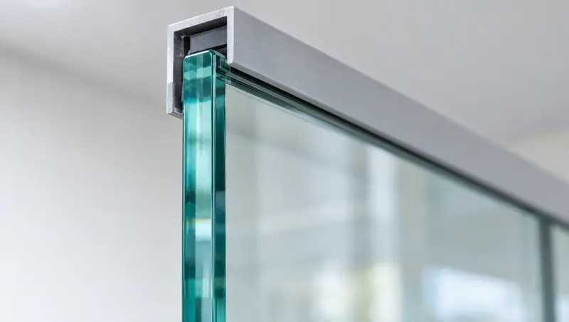 Toughened glass edge in an aluminium channel. Green-tinted edge of a toughened glass panel meeting an aluminium channel (illustrative)